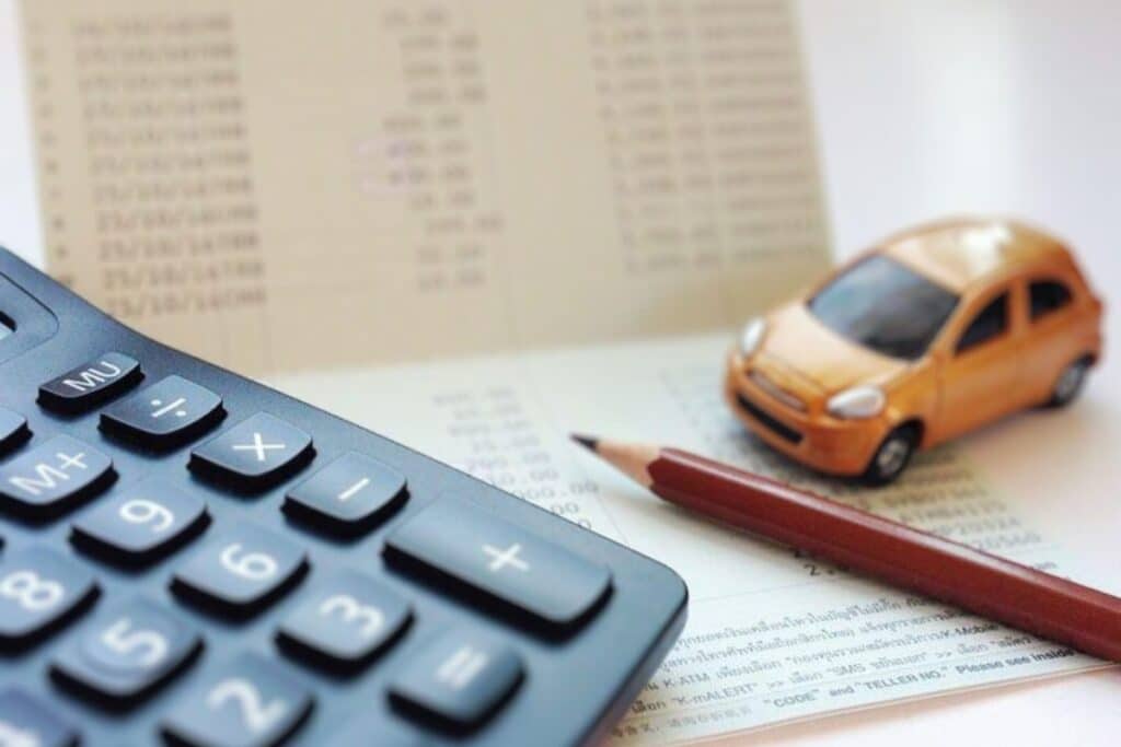 Calculadora, lápis e miniatura de carro sobre documento financeiro.